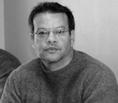 A man with glasses and a sweater is sitting.