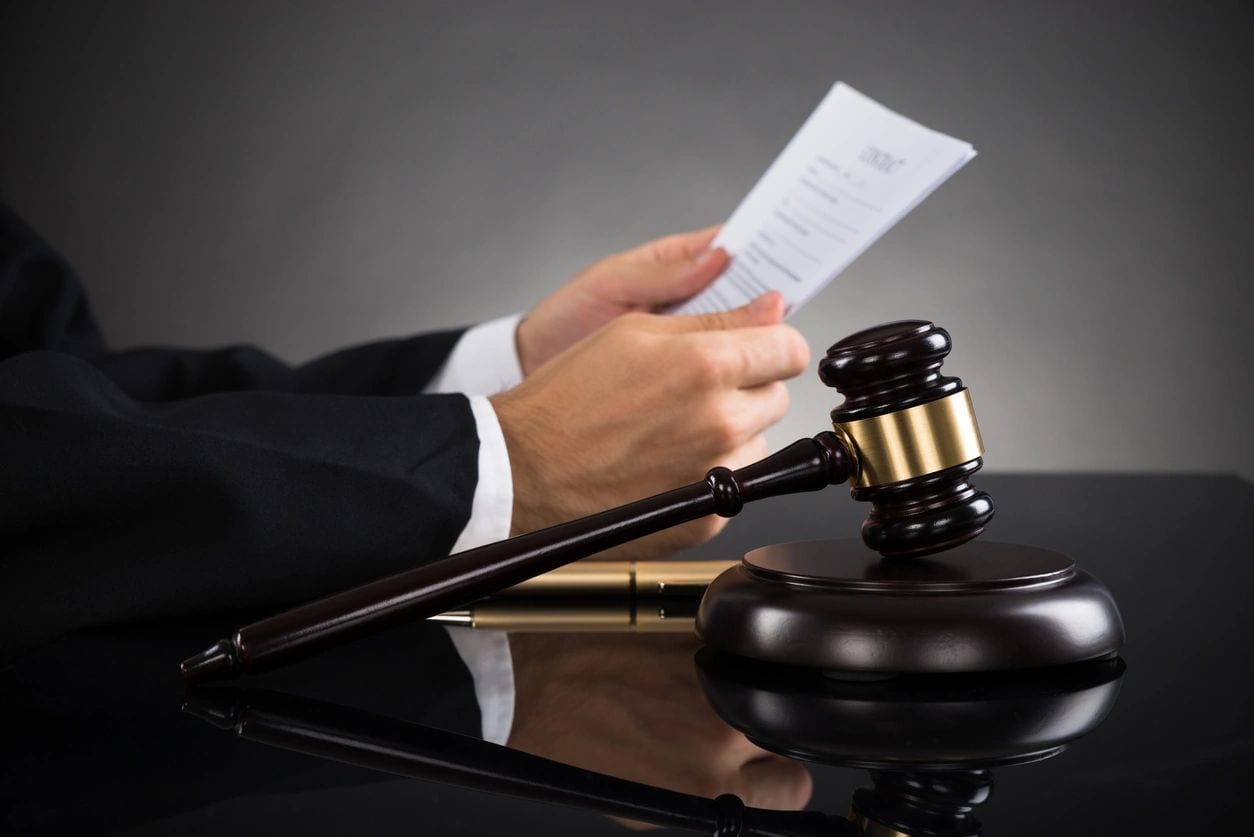 A judge holding papers and gavel on top of table.